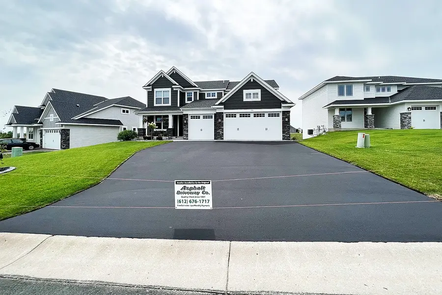 New asphalt driveway in front of a two-storey home with an Asphalt Driveway Co. yard sign
