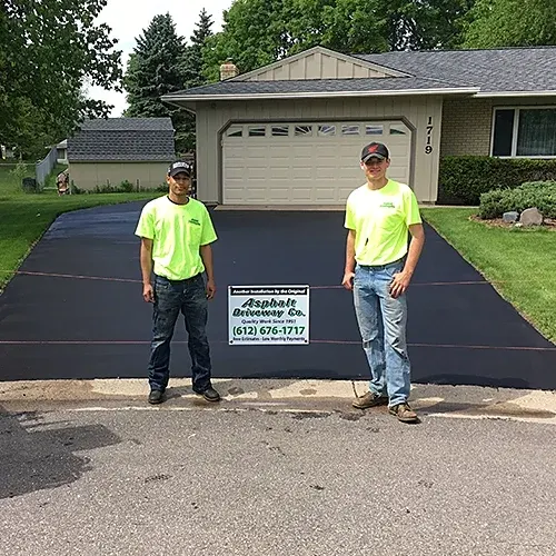 Two Asphalt Driveway Co. crew members on a freshly sealed driveway
