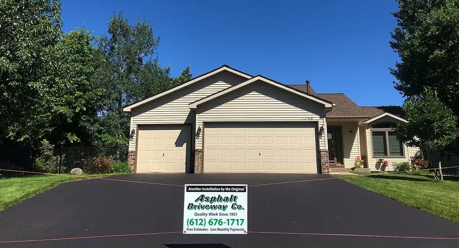 New asphalt driveway at a rambler with an Asphalt Driveway Co. yard sign